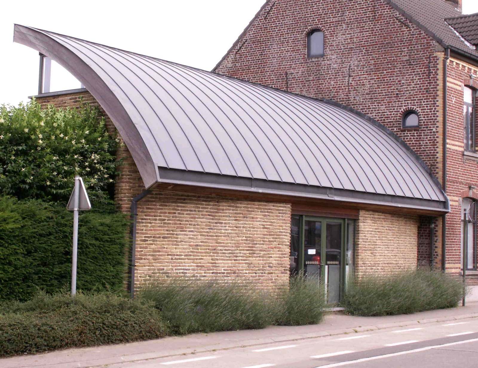 Gebouw met een gebogen metalen dak naast een bakstenen woning